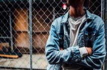 Crop black trendy serious male with silver chain on neck in blue denim jacket looking away on street — Stock Photo