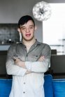 Smiling Latin teenage boy with Down syndrome standing with crossed arms in room at home and looking at camera — Stock Photo