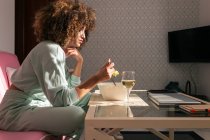 Vista laterale dell'insalata femminile afroamericana mentre siede a tavola con un bicchiere di vino e pranza gustosa a casa — Foto stock
