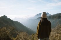 Visão traseira da mulher irreconhecível em roupas quentes de pé sozinho no miradouro e olhando para cumes de montanha nebulosos cobertos de nuvens fofas no Parque Nacional Sequoia sob o céu azul nos EUA — Fotografia de Stock