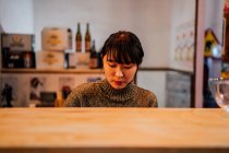 Giovane donna asiatica in abbigliamento casual seduta al bancone di legno in attesa di ordine in ramen bar — Foto stock