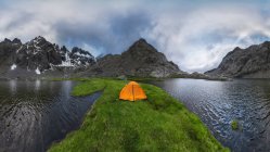 Orange tent located on grassy shore of Laguna Grande lake against Sierra de Gredos mountain range and cloudy sky in Avila, Spain — Stock Photo
