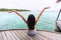 Back view of unrecognizable female in casual clothes sitting on wooden pier relaxing in Maldives — Stock Photo