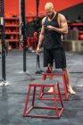 Sportivo calvo muscolare in piedi in palestra moderna navigando sullo smartphone durante la pausa allenamento — Foto stock