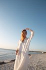 Mulher loira de cabelos compridos em pé na praia olhando para a distância — Fotografia de Stock