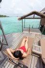 Зверху жінка з головою у купальнику лежить на палубному стільці, відпочиваючи на Мальдівах. — стокове фото