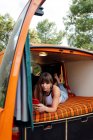 Feminino viajante deitado na cama em van e usando telefone celular durante a viagem no verão — Fotografia de Stock