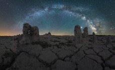 Magnificent landscape with glowing Milky Way in night starry sky over dry desert barren terrain with rocky formations — Stock Photo