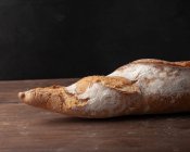 Appetizing freshly baked baguette with crispy crust placed on wooden table against black background — Stock Photo