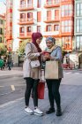 Мусульманські жінки - друзі в хіджабах і з паперовими сумками, які користуються смартфоном на вулиці після покупки. — стокове фото