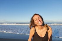 Lächelnde Frau im Sommerkleid steht am Sandstrand und blickt in die Kamera — Stockfoto