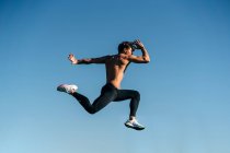 Vue latérale de l'athlète masculin actif en vêtements de sport sautant pendant l'entraînement cardio au soleil — Photo de stock