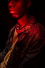 Урожай спокойный стильный афроамериканец в джинсовой куртке под неоновым красным светом в тени на черном фоне, смотрящий в камеру — стоковое фото