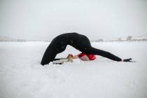 Seitenansicht der anmutigen Frau praktiziert Yoga in Kapotasana auf schneebedecktem Feld im Winter — Stockfoto