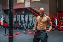 Muskulöser bärtiger Mann zieht beim funktionellen Training im modernen Fitnessstudio mit Mühe ein elastisches Seil — Stockfoto