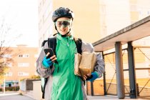 Frohe Zustellerin mit eingepackten Kartons und GPS-Karte auf dem Handy, während sie an sonnigen Tagen auf der Straße steht — Stockfoto
