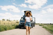 Inquiète jeune femme afro-américaine avec les cheveux bouclés parler sur téléphone portable tout en demandant de l'aide du service de réparation après un accident avec camping-car dans la campagne — Photo de stock