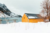 Cabina amarilla situada cerca de la cordillera costera nevada en las Islas Lofoten, Noruega - foto de stock