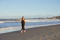 Pieno corpo femminile sorridente in abito estivo in piedi sulla spiaggia di sabbia e guardando altrove — Foto stock