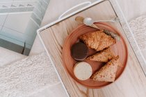 Blick von oben auf Sandwich-Kekse und Croissant auf Teller serviert mit Getreidebrot auf Tablett zum Frühstück auf dem Bett — Stockfoto