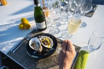 Délicieux et bien décoré plat d'huîtres jumelé avec du champagne au restaurant de haute cuisine en plein air tandis que la main tient verre de champagne — Photo de stock