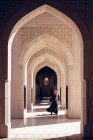 Volle Länge einer unkenntlichen Frau in traditioneller Kleidung, die durch den ornamentalen Torbogen der Großen Sultan-Qaboos-Moschee in Maskat geht — Stockfoto
