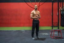 Ganzkörperkräftiger bärtiger Mann, der wegschaut und denkt, während er beim Training in einem modernen Fitnessstudio in der Nähe von Geräten steht — Stockfoto