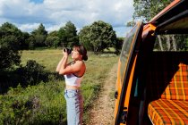 Delighted traveling female photographer taking pictures on professional camera during vacation in woods — Stock Photo
