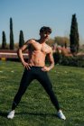 Hemdloser männlicher Athlet mit Tätowierung und breiten Beinen beim Training auf der Wiese — Stockfoto