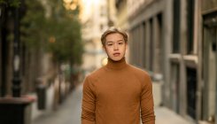 Modelo masculino étnico confiante com cabelo loiro e gola alta na moda em pé na cidade e olhando para a câmera — Fotografia de Stock