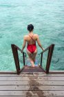 Vista trasera de la mujer anónima en traje de baño que baja por las escaleras en el agua relajante en Maldivas - foto de stock