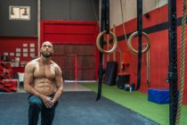 Muskulöser bärtiger Mann blickt beim Training im modernen Fitnessstudio neben Geräten auf — Stockfoto