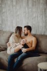 Homem e mulher felizes com caneca de bebida quente sorrindo e olhando um para o outro enquanto passam o tempo em casa de manhã — Fotografia de Stock