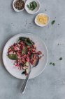 Vista dall'alto di piatti e ciotola con deliziosa insalata di lenticchie con cetrioli e spinaci posizionati vicino a tovaglioli sul tavolo grigio — Foto stock