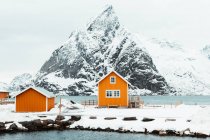 Желтые домики, расположенные рядом с горным хребтом заснеженного морского побережья на Лофских островах, Норвегия — стоковое фото