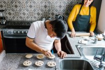 Alto ángulo de adolescente latino con síndrome de Down decorando galletas crudas con chips de chocolate mientras cocina en casa - foto de stock