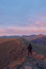 Visão traseira do caminhante anônimo em pé na colina rochosa nas terras altas e desfrutando de vista do cume da montanha ao pôr do sol no País de Gales — Fotografia de Stock