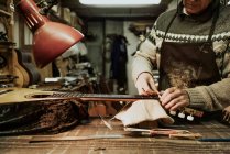 Crop anonymous male luthier in sweater measuring fret nut while repairing acoustic guitar at workshop — Stock Photo