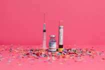 Frasco de vacuna contra el Coronavirus cerca de análisis de sangre y jeringa sobre fondo rosa cubierto de confeti - foto de stock