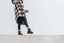 Unrecognizable woman in trendy checkered coat balancing on border while walking against gray wall on street — Stock Photo