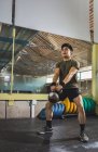 Asiatischer Mann trainiert Schultern und Arme mit schweren Kettlebells im Fitnessstudio während des funktionellen Trainings und schaut weg — Stockfoto