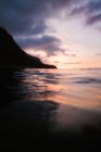 Blaues Meer, das während des Sonnenuntergangs über die Küste in der Nähe eines entfernten Berges rollt — Stockfoto