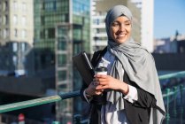 Cheerful Muslim female entrepreneur in hijab and with takeaway coffee standing in street — Stock Photo