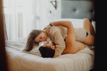 Allegro giovane uomo e donna sorridenti e coccole mentre sdraiati su un comodo letto a casa insieme — Foto stock