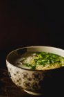 Chinese ramen meal in ceramic bowl with oriental ornament placed on wooden table on black background — Stock Photo