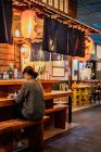 Азиатка в обычном свитере с помощью мобильного телефона у стойки в традиционном рамен-баре — стоковое фото