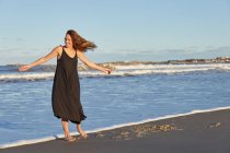 Corpo inteiro sorridente feminino em vestido de verão em pé na praia arenosa e olhando para longe — Fotografia de Stock