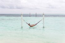 Frau in rotem Badeanzug liegt in Hängematte und schwingt sich an bewölkten Tagen auf den Malediven über die Surfleine — Stockfoto