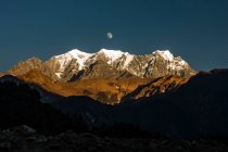 Picos del Himalaya de pintoresca cresta montañosa ubicada contra el cielo al atardecer con nubes y luna por la noche en Nepal - foto de stock
