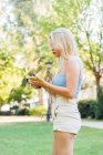 Side view of peaceful female in summer clothes listening to music in earphones while standing in park — Stock Photo